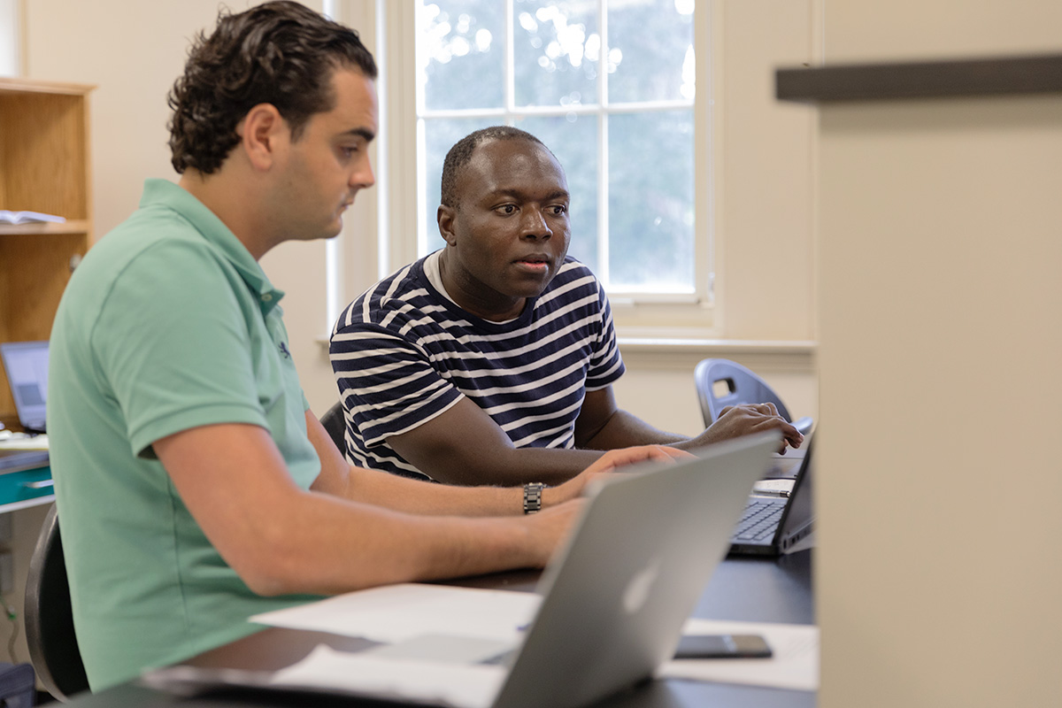 Two students collaborate while working on laptops. 